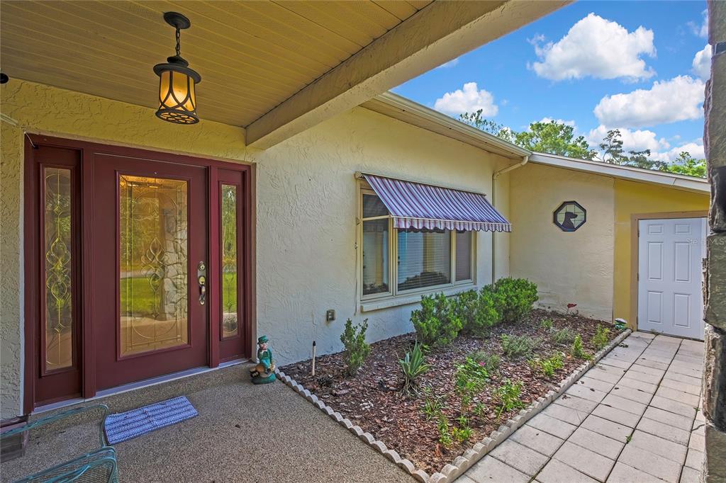 A front porch with a red door, a striped window awning, and a landscaped garden bed — 12 MAYFLOWER COURT E, HOMOSASSA, FL