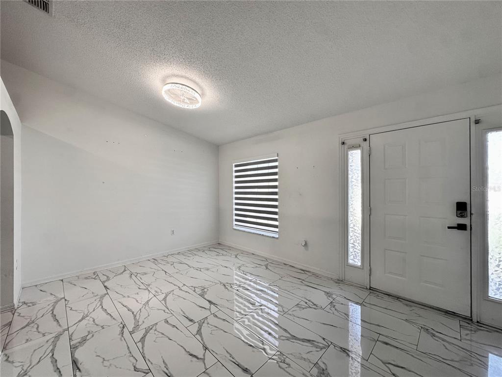 An empty room features white walls, a ceiling light, a window with blinds, and marble flooring — 3190 AMBASSADOR AVENUE, SPRING HILL, FL