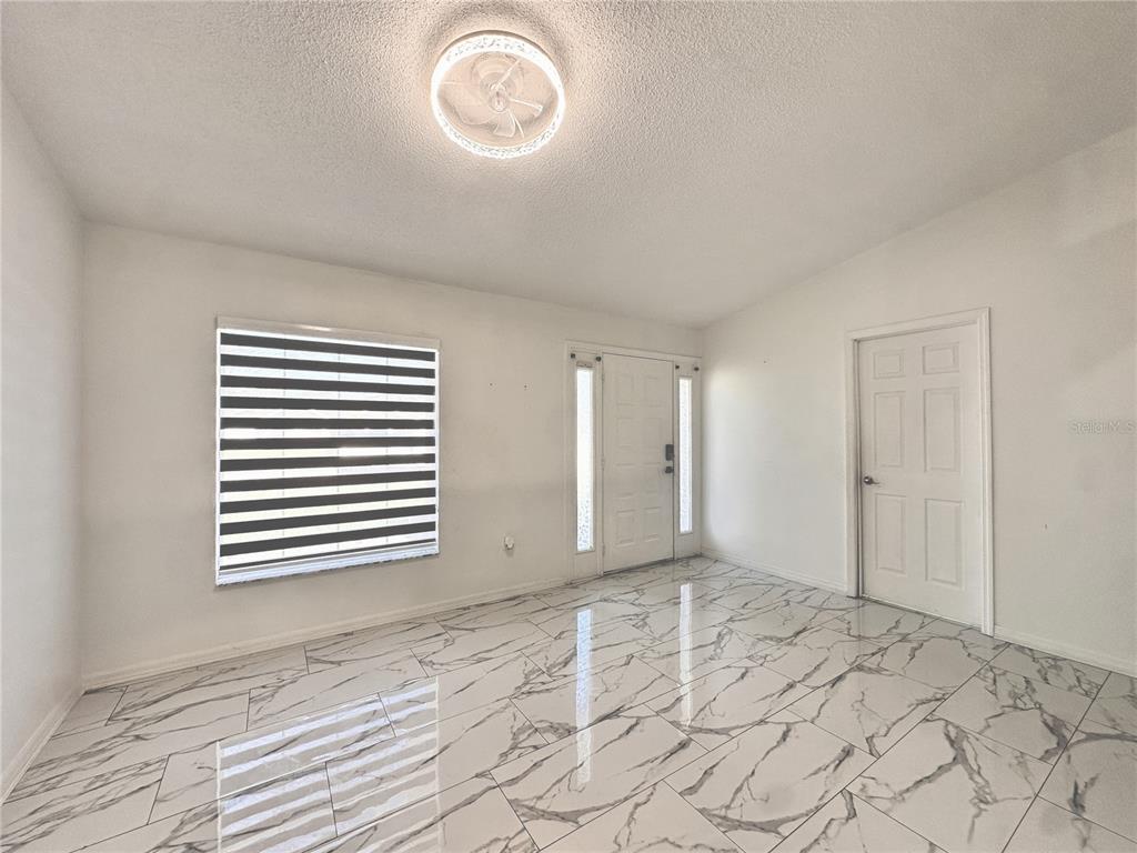 An entryway features white walls, a ceiling fan light fixture, and white marble-patterned tile flooring — 3190 AMBASSADOR AVENUE, SPRING HILL, FL
