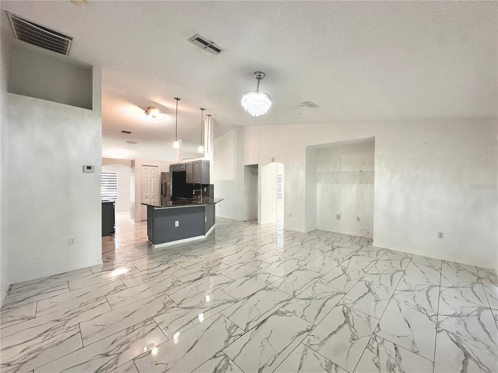 An open-concept living area features white marble-look tile flooring and a kitchen with dark cabinetry — 3190 AMBASSADOR AVENUE, SPRING HILL, FL