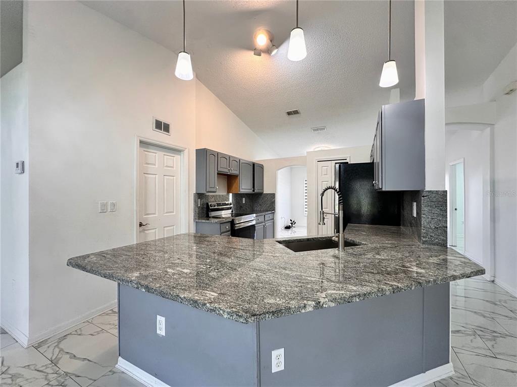 A kitchen features gray cabinets, granite countertops, a breakfast bar, and white tile flooring — 3190 AMBASSADOR AVENUE, SPRING HILL, FL