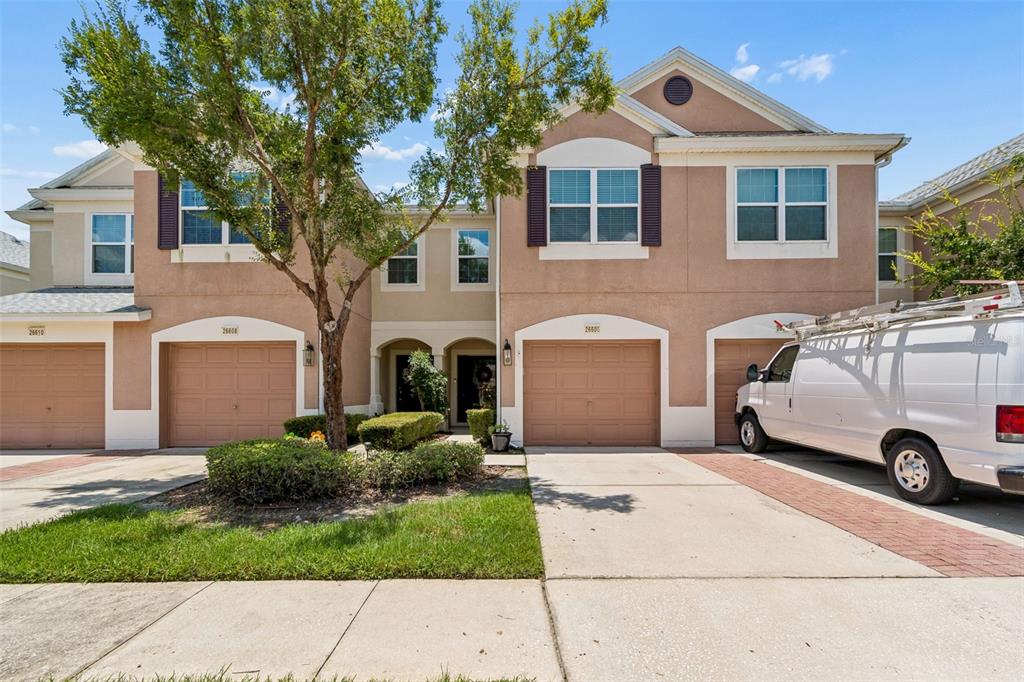 A two-story townhouse exterior features tan stucco walls, brown garage doors, and a white van — 26606 CASTLEVIEW WAY, WESLEY CHAPEL, FL