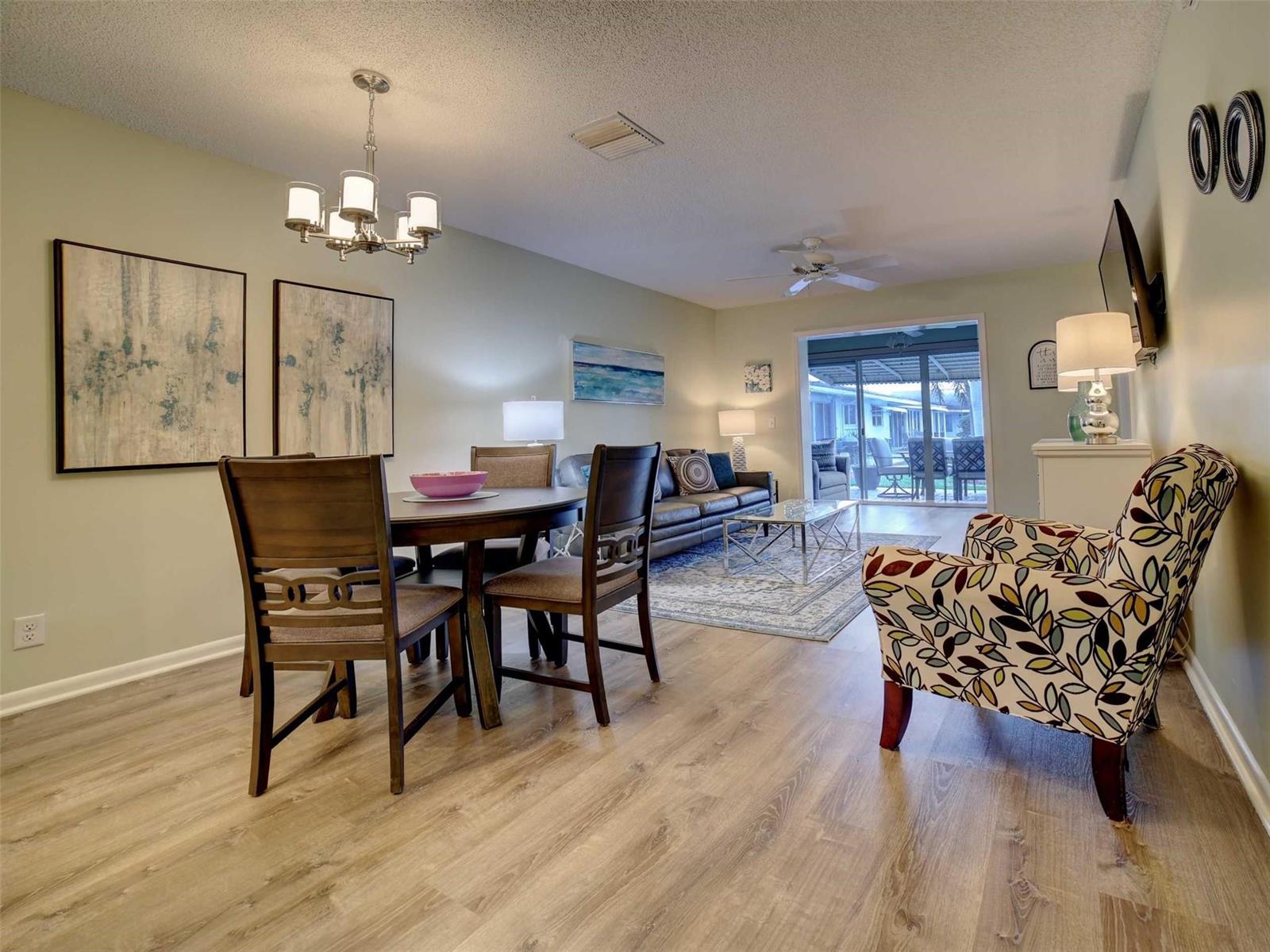 An open-concept living and dining room with wood-look flooring, a chandelier, and a sliding door — 400 SW Golfview Terrace # 111, Boynton Beach FL 33426, BOYNTON BEACH, FL