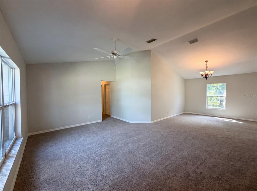 A spacious living room features vaulted ceilings, beige carpeting, a ceiling fan, and a chandelier — 517 BAHIA CIRCLE RUN, OCALA, FL