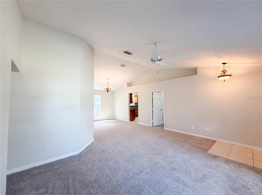 A spacious living area features beige carpeting, vaulted ceilings, a ceiling fan, and light walls — 517 BAHIA CIRCLE RUN, OCALA, FL