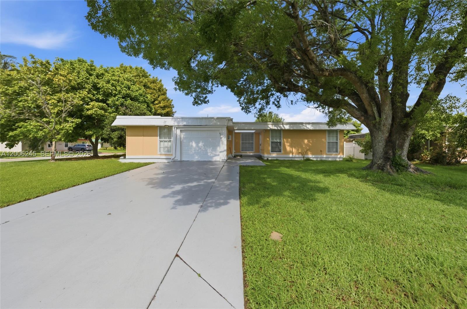 A single-story yellow house with a white garage door and a large tree in front — TAMARAC, FL