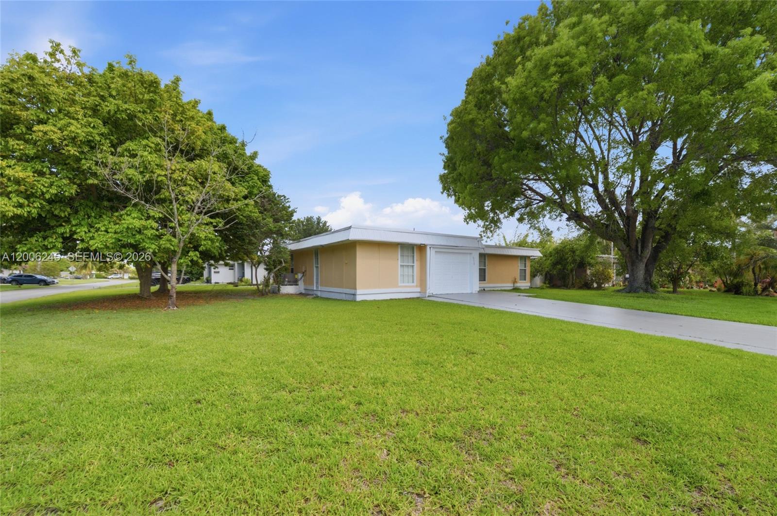 A single-story house with a yellow exterior and a concrete driveway sits on a lawn — TAMARAC, FL