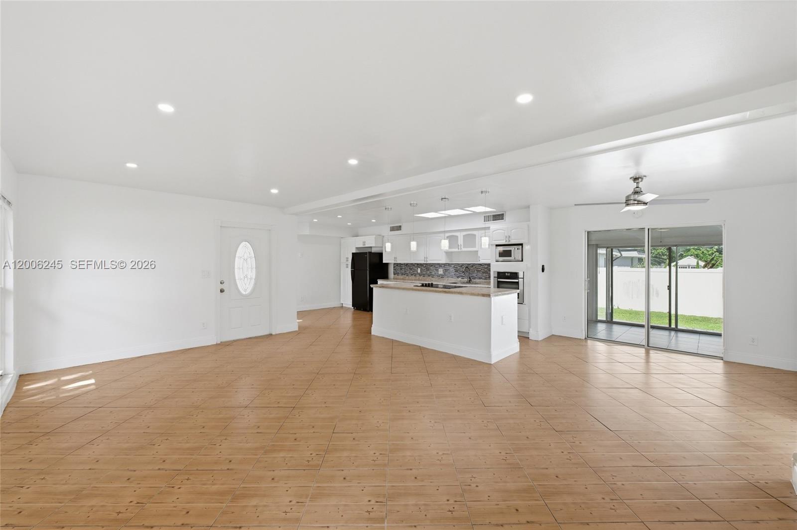 An open-concept kitchen with white cabinetry and an island overlooks a spacious tiled living area — TAMARAC, FL