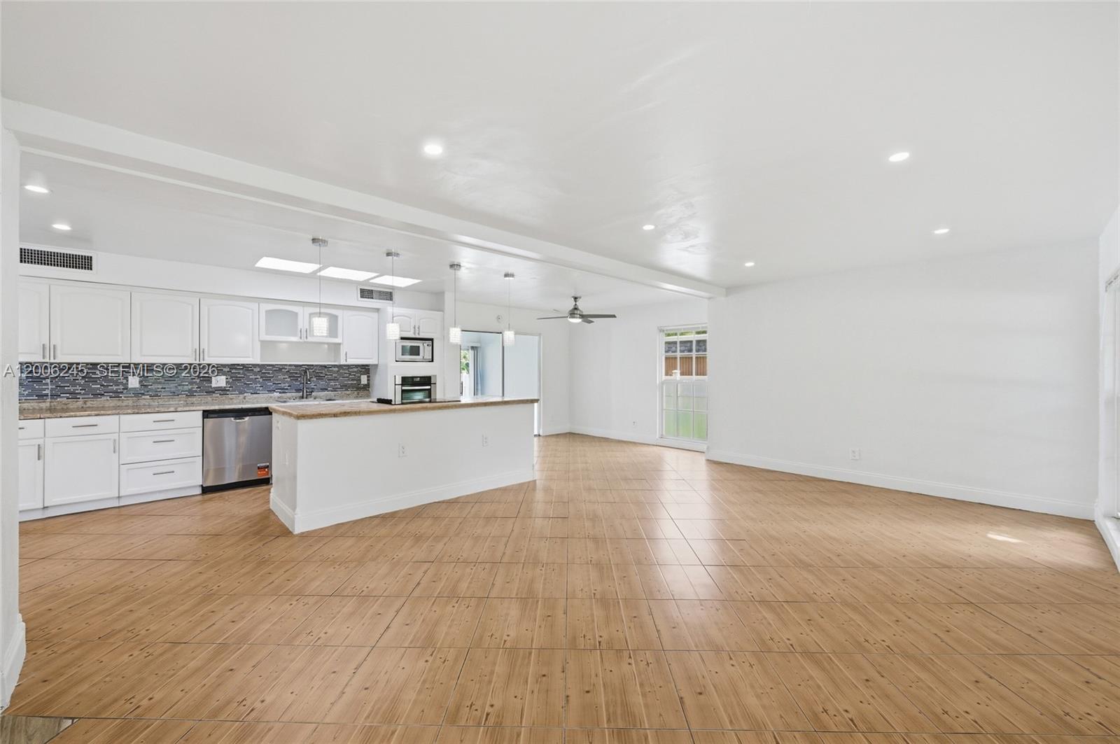 A kitchen with white cabinets and a breakfast bar opens into a large living area — TAMARAC, FL