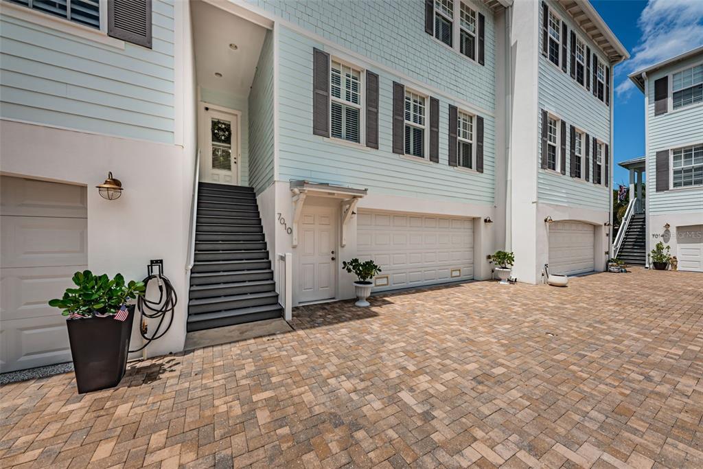 The exterior of a multi-story house features light blue siding, a paver driveway, and garages — 7010 GREVILLA AVENUE S, SOUTH PASADENA, FL