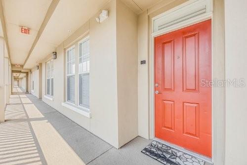 An exterior view of a building hallway featuring a bright orange door and large windows — 1410 CELEBRATION AVENUE UNIT 407, CELEBRATION, FL