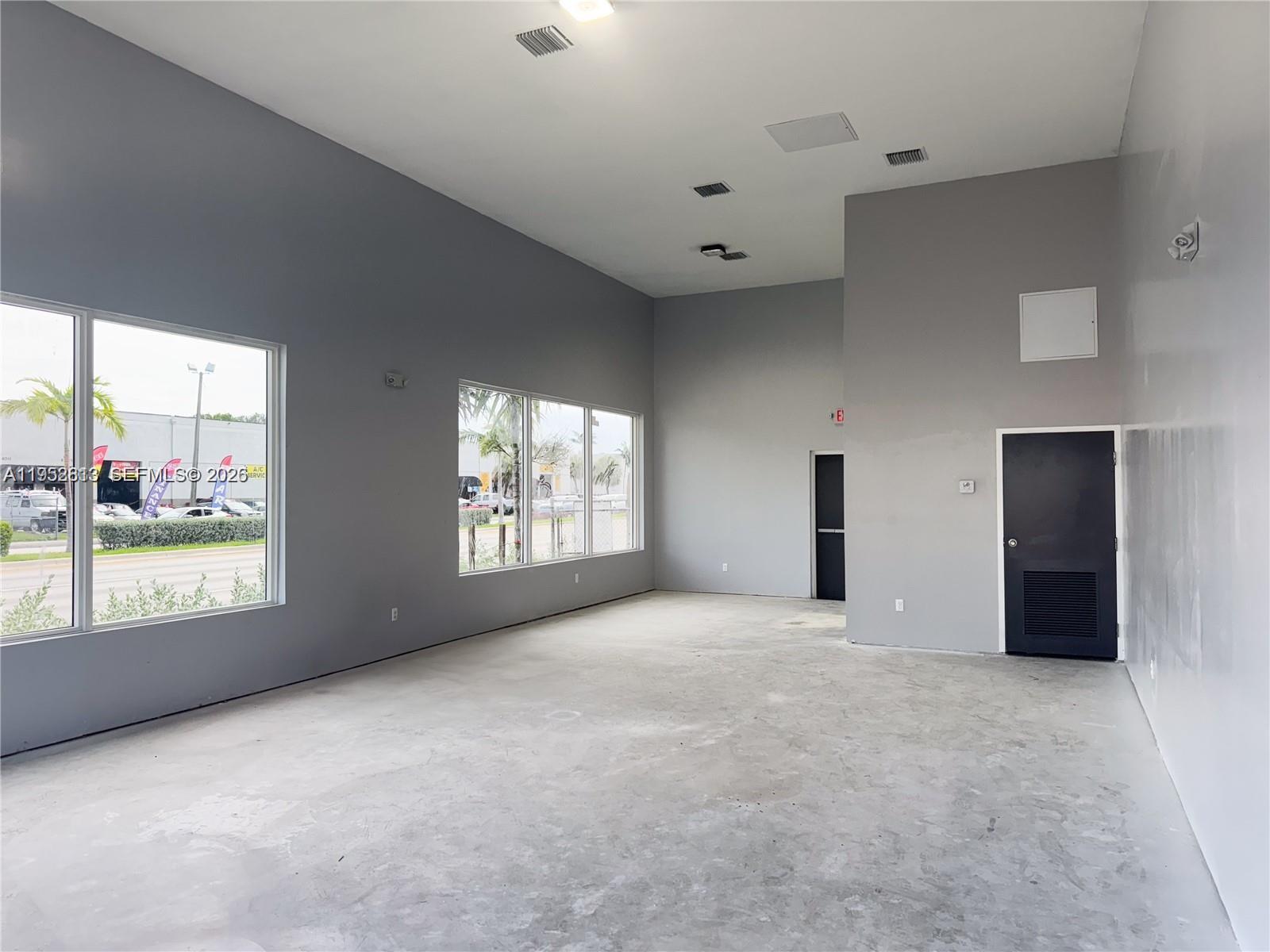 An empty commercial space features gray walls, concrete floors, large windows, and two dark doors — 4030 Pembroke Rd, Hollywood FL 33021, HOLLYWOOD, FL