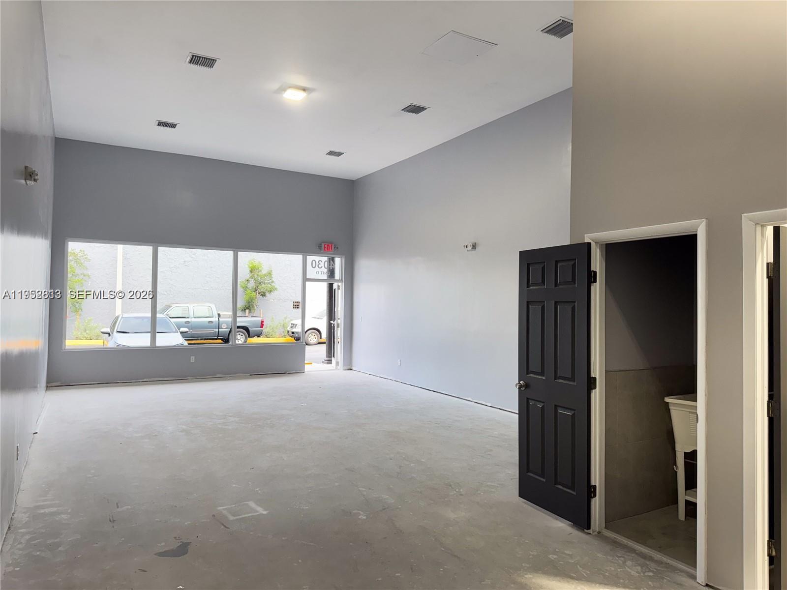 An empty commercial space features high ceilings, gray walls, concrete floors, and a small restroom — 4030 Pembroke Rd, Hollywood FL 33021, HOLLYWOOD, FL