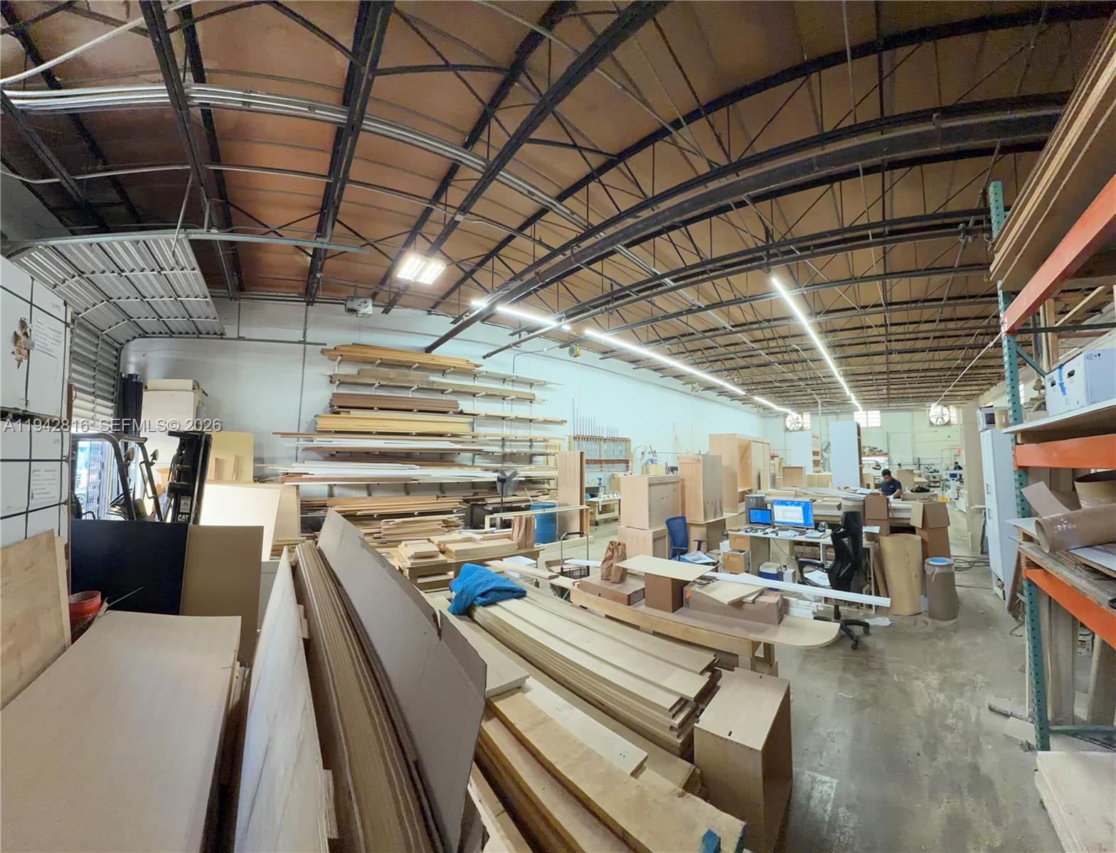 This industrial warehouse space features high ceilings, exposed metal trusses, and extensive wood material storage — 733 W 26th St # 733, Hialeah FL 33010, HIALEAH, FL