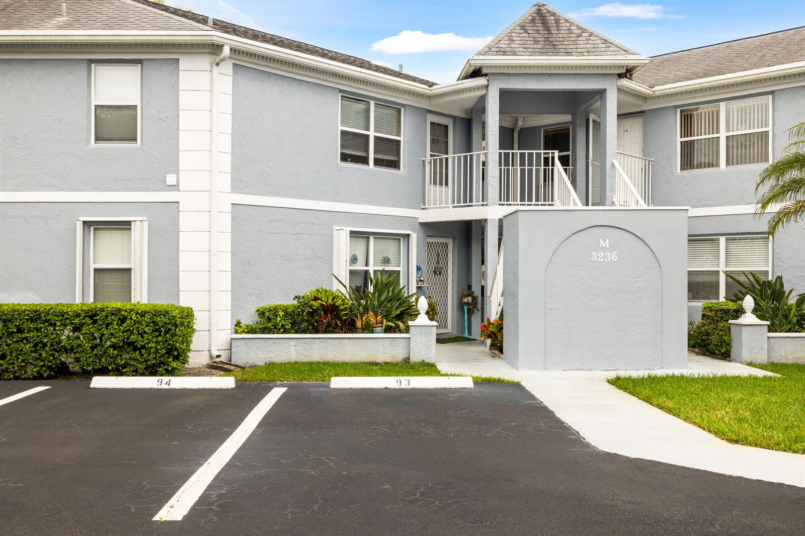 A two-story blue apartment building features a covered entryway, a second-floor balcony, and parking spaces — 3236 SE Aster Lane # M226, Stuart FL 34994, STUART, FL