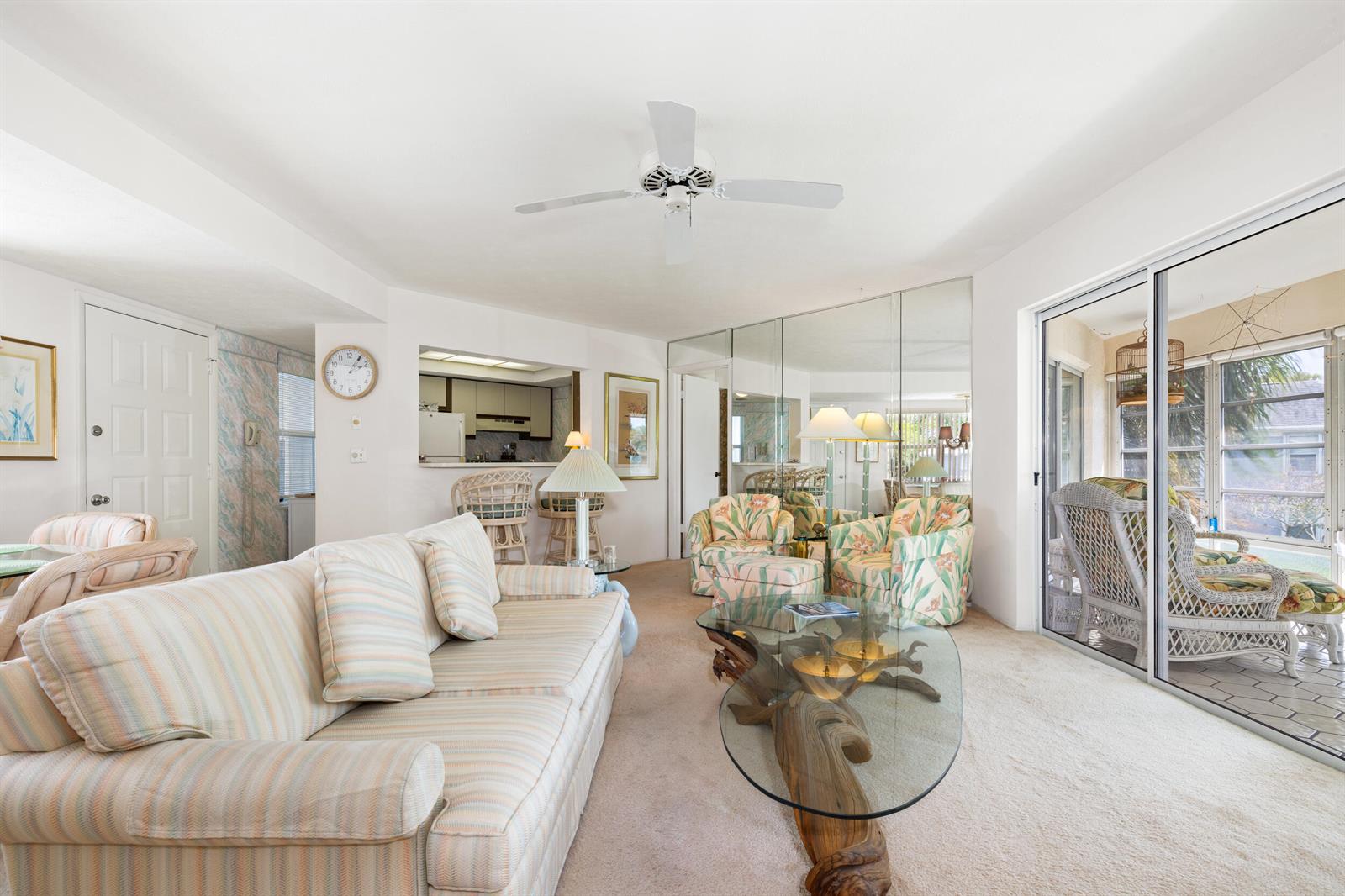 A living room features a striped sofa, a glass-topped driftwood table, and mirrored wall panels — 3236 SE Aster Lane # M226, Stuart FL 34994, STUART, FL