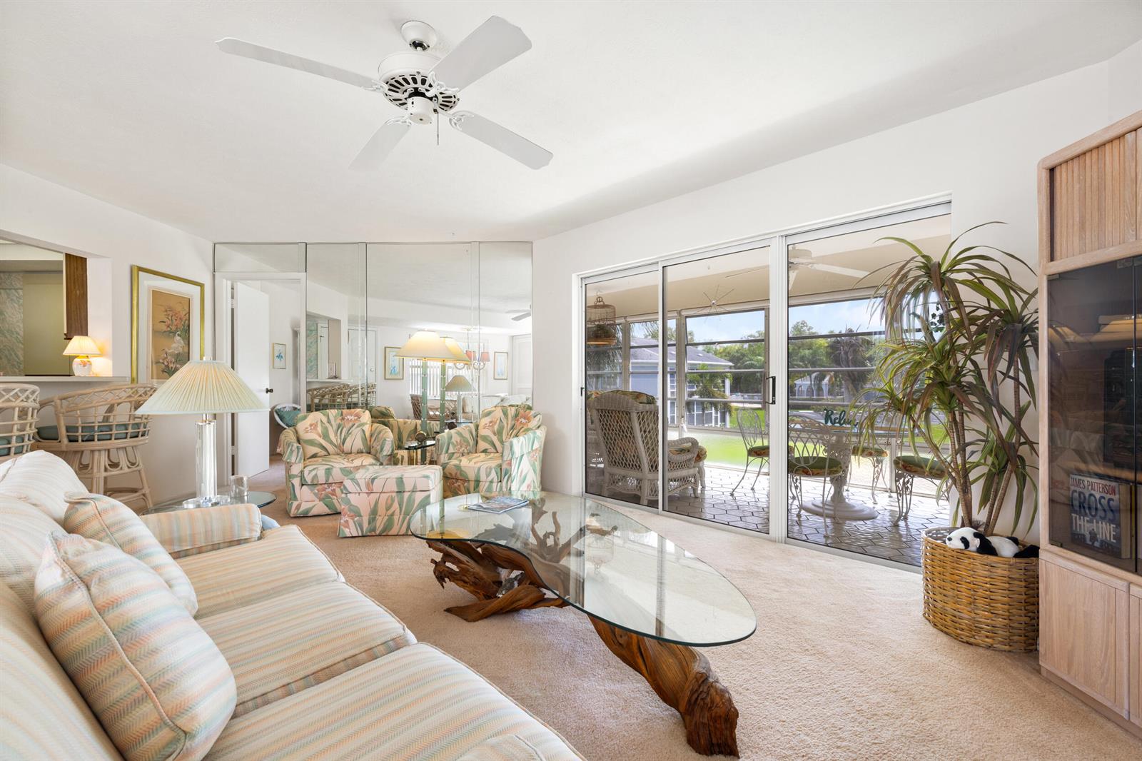A living room features a glass-topped driftwood coffee table, patterned furniture, and a sliding glass door — 3236 SE Aster Lane # M226, Stuart FL 34994, STUART, FL