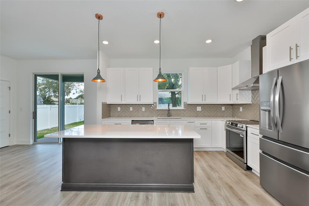 A kitchen features a dark gray island, white cabinets, stainless steel appliances, and wood-look flooring — 4171 56TH AVENUE N, ST PETERSBURG, FL
