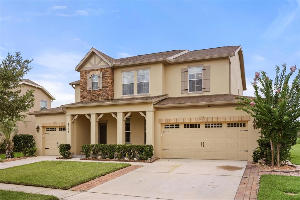A two-story suburban house with a tan stucco exterior, stone accents, and a three-car garage — 3018 BOATING BOULEVARD, KISSIMMEE, FL