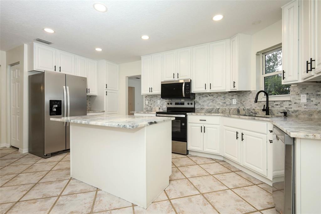 A kitchen with white cabinets, stainless steel appliances, a center island, and stone countertops — 1636 TUSCALOOSA AVENUE, HOLLY HILL, FL