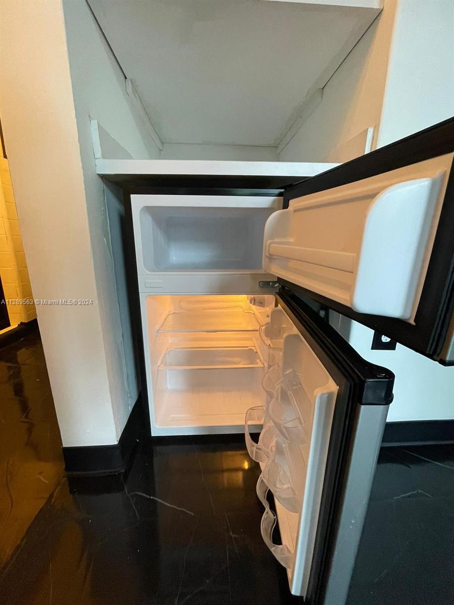 A small refrigerator is installed in a recessed wall niche with black flooring — 1455 Michigan Ave # 7, Miami Beach FL 33139, MIAMI BEACH, FL