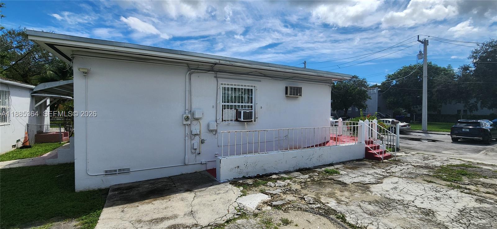 The exterior of a white, single-story building features a concrete patio with a metal railing — 405 NW 64th St, Miami FL 33150, MIAMI, FL
