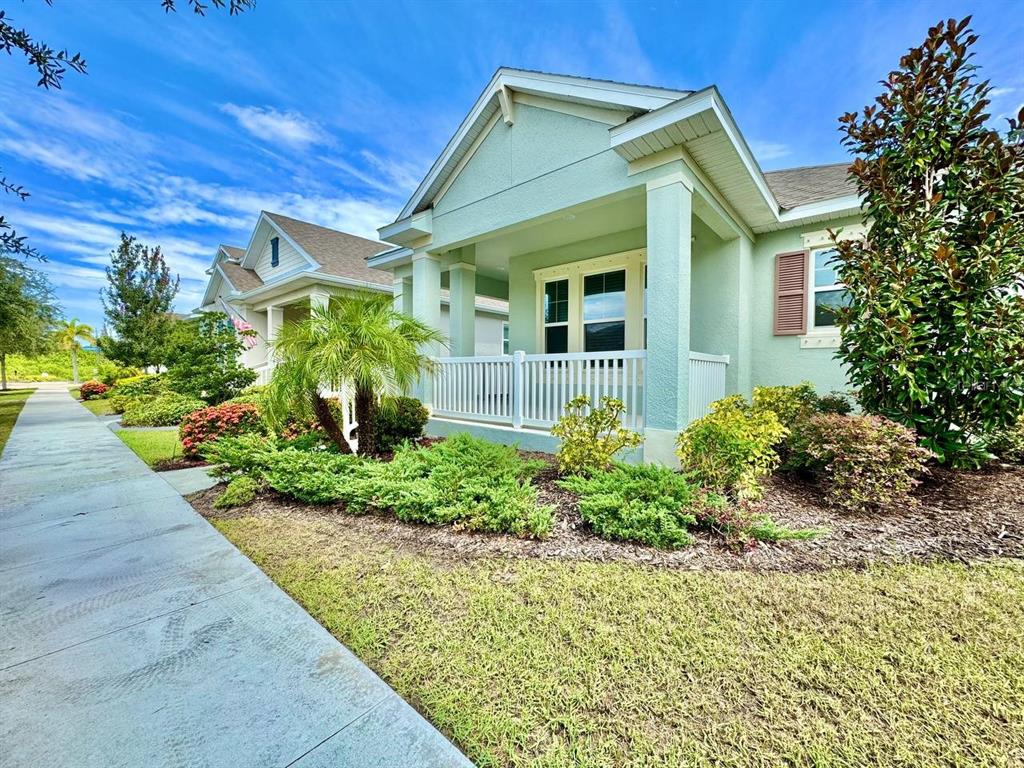 A light green house with a front porch and white railing sits beside a sidewalk — 827 WINTERSIDE DRIVE, APOLLO BEACH, FL