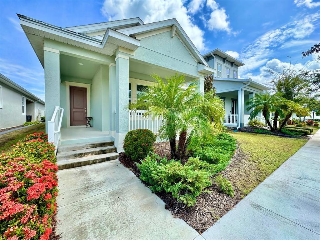 A light green house with a front porch, palm tree, and red flowers — 827 WINTERSIDE DRIVE, APOLLO BEACH, FL