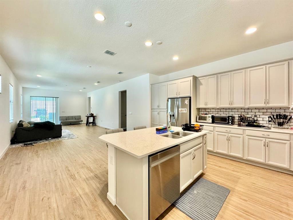 A kitchen with an island and stainless steel appliances opens into a living area — 827 WINTERSIDE DRIVE, APOLLO BEACH, FL