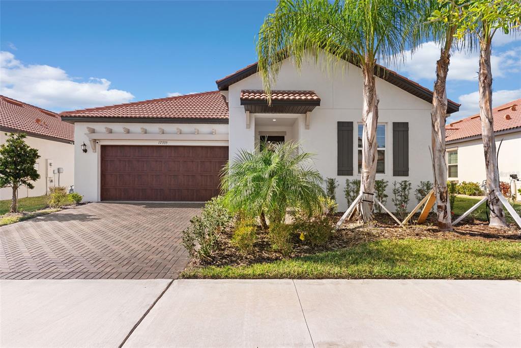 A single-story house with a brown garage door, tiled roof, and palm trees in front — 17335 HOLLY WELL AVENUE, WIMAUMA, FL