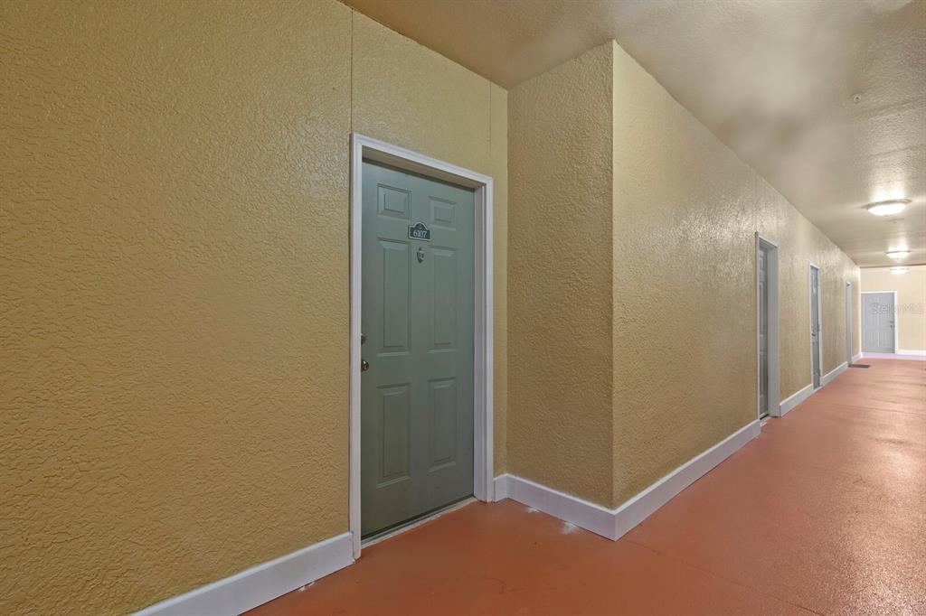 A long apartment hallway features tan textured walls, a green door, and orange flooring — 4207 S DALE MABRY HIGHWAY UNIT 6107, TAMPA, FL