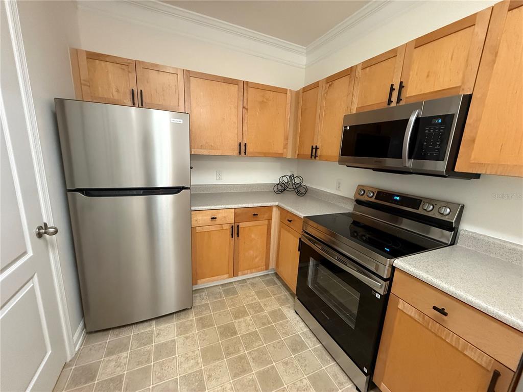 A kitchen features light wood cabinets, stainless steel appliances, and light-colored countertops — 8801 VILLA VIEW CIRCLE UNIT 202, ORLANDO, FL