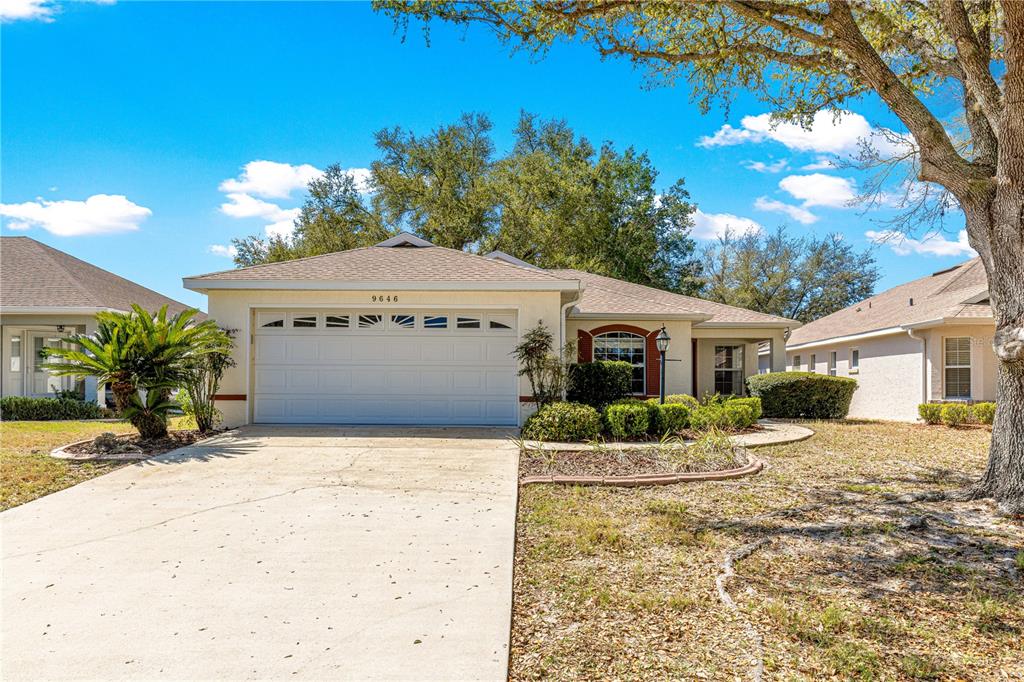 A single-story house with a beige stucco exterior, a two-car garage, and a concrete driveway — 9646 SW 92ND PLACE ROAD, OCALA, FL