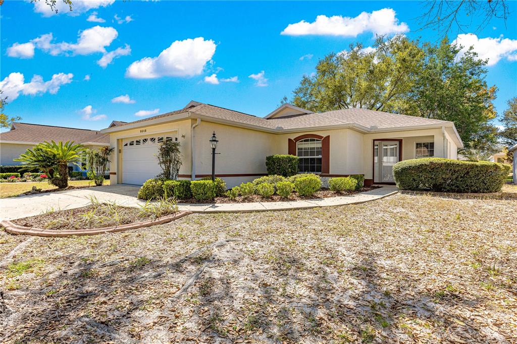 A single-story house with a beige stucco exterior, a two-car garage, and a landscaped yard — 9646 SW 92ND PLACE ROAD, OCALA, FL