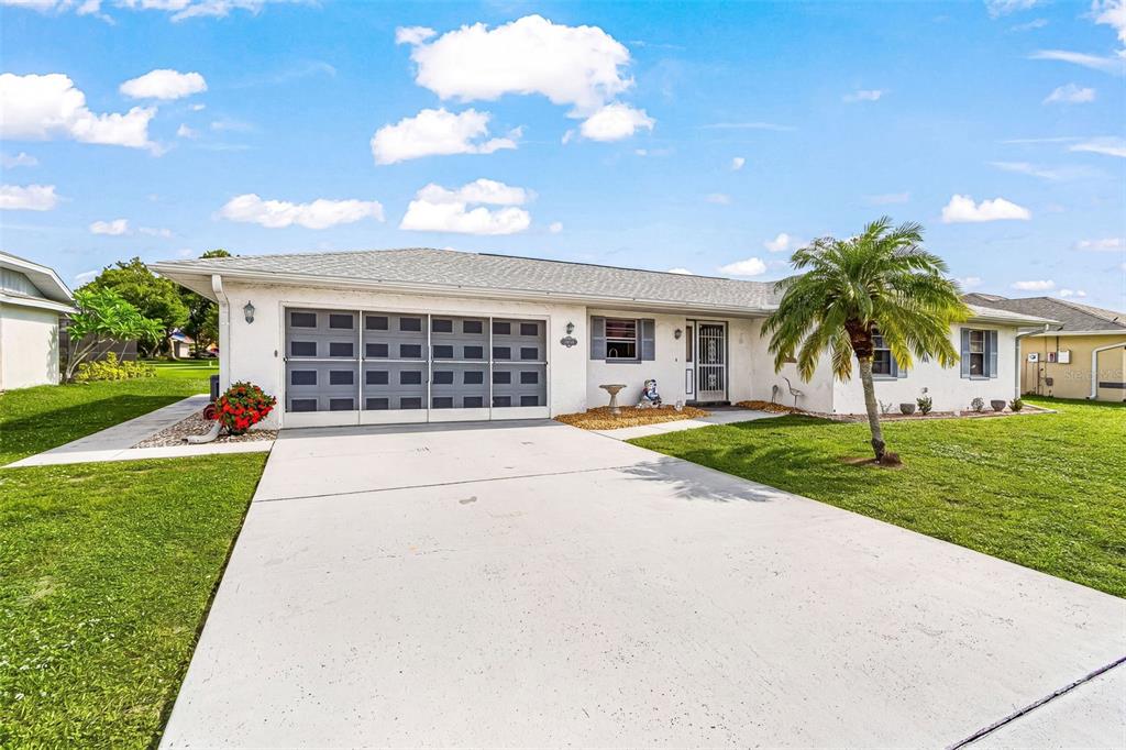 A single-story house with a white exterior, a gray garage door, and a palm tree — 26058 DEEP CREEK BOULEVARD, PUNTA GORDA, FL