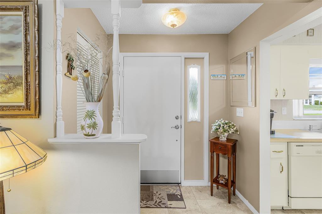 An entryway features a white front door, tile flooring, a small wooden table, and a half-wall — 26058 DEEP CREEK BOULEVARD, PUNTA GORDA, FL