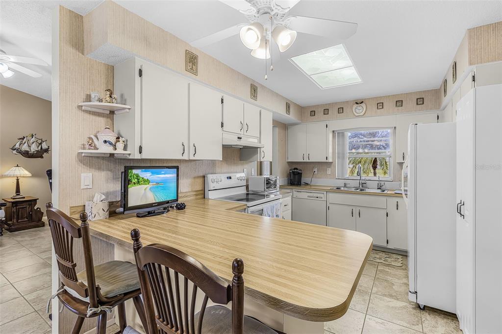 A kitchen with white cabinets, wood-look laminate countertops, and a breakfast bar with two chairs — 26058 DEEP CREEK BOULEVARD, PUNTA GORDA, FL