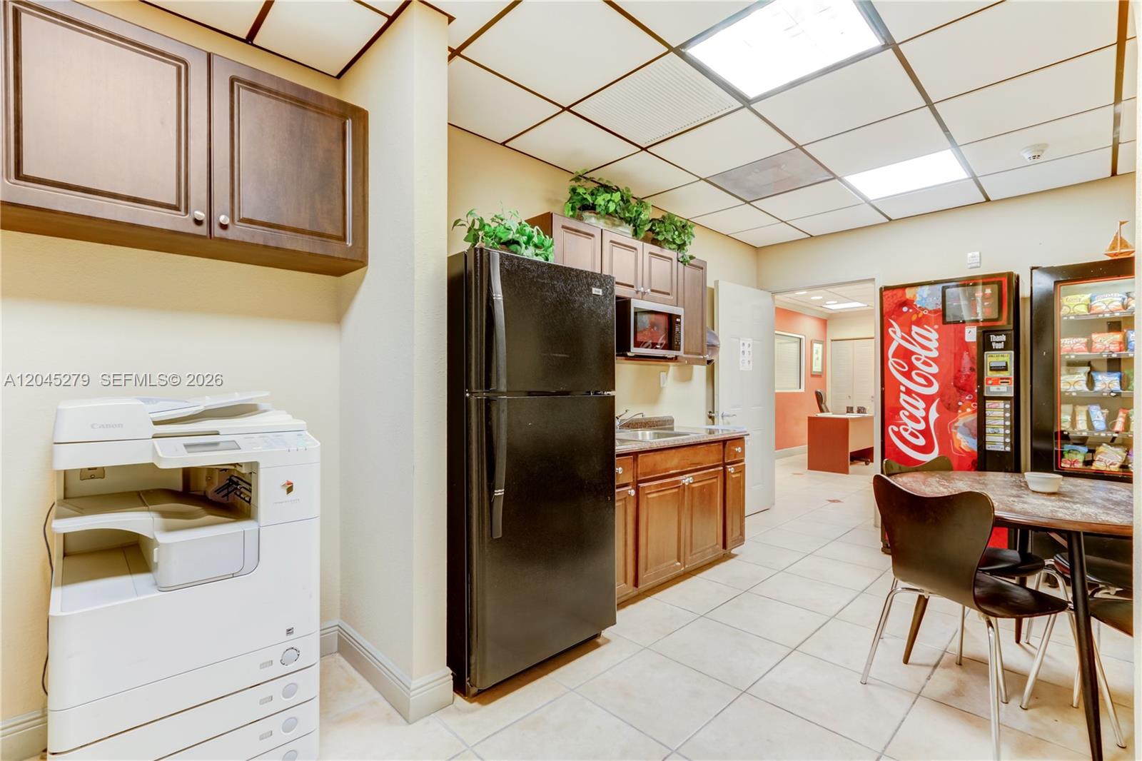 This breakroom features a black refrigerator, kitchenette cabinetry, a printer, and two vending machines — 12150 SW 128th Ct # 107, Miami FL 33186, MIAMI, FL
