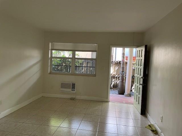 An empty room with beige tile flooring, a window air conditioner, and an open door — MIAMI BEACH, FL