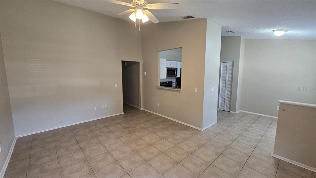 An open-concept living area features beige walls, tile flooring, and a ceiling fan — 1501 KESTREL WAY, BRANDON, FL