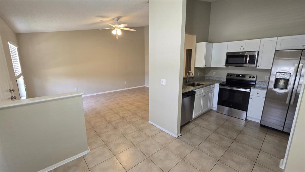 A kitchen with white cabinets and stainless steel appliances opens into a living area — 1501 KESTREL WAY, BRANDON, FL
