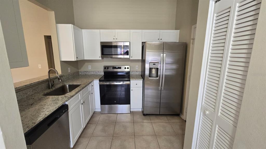 A kitchen features white cabinets, granite countertops, stainless steel appliances, and light-colored tile flooring — 1501 KESTREL WAY, BRANDON, FL