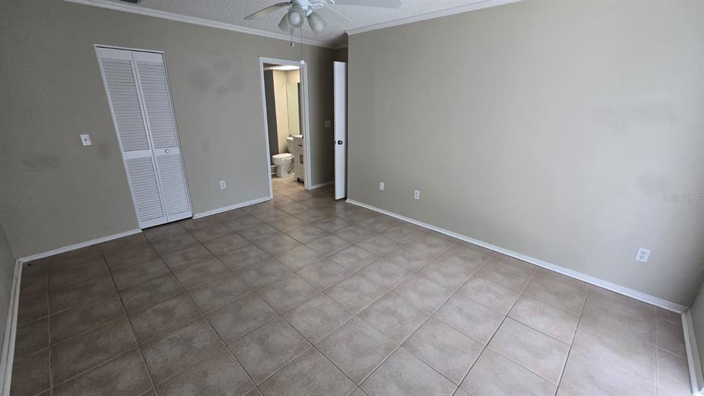 An empty bedroom features beige walls, light-colored tile flooring, a ceiling fan, and a closet — 1501 KESTREL WAY, BRANDON, FL