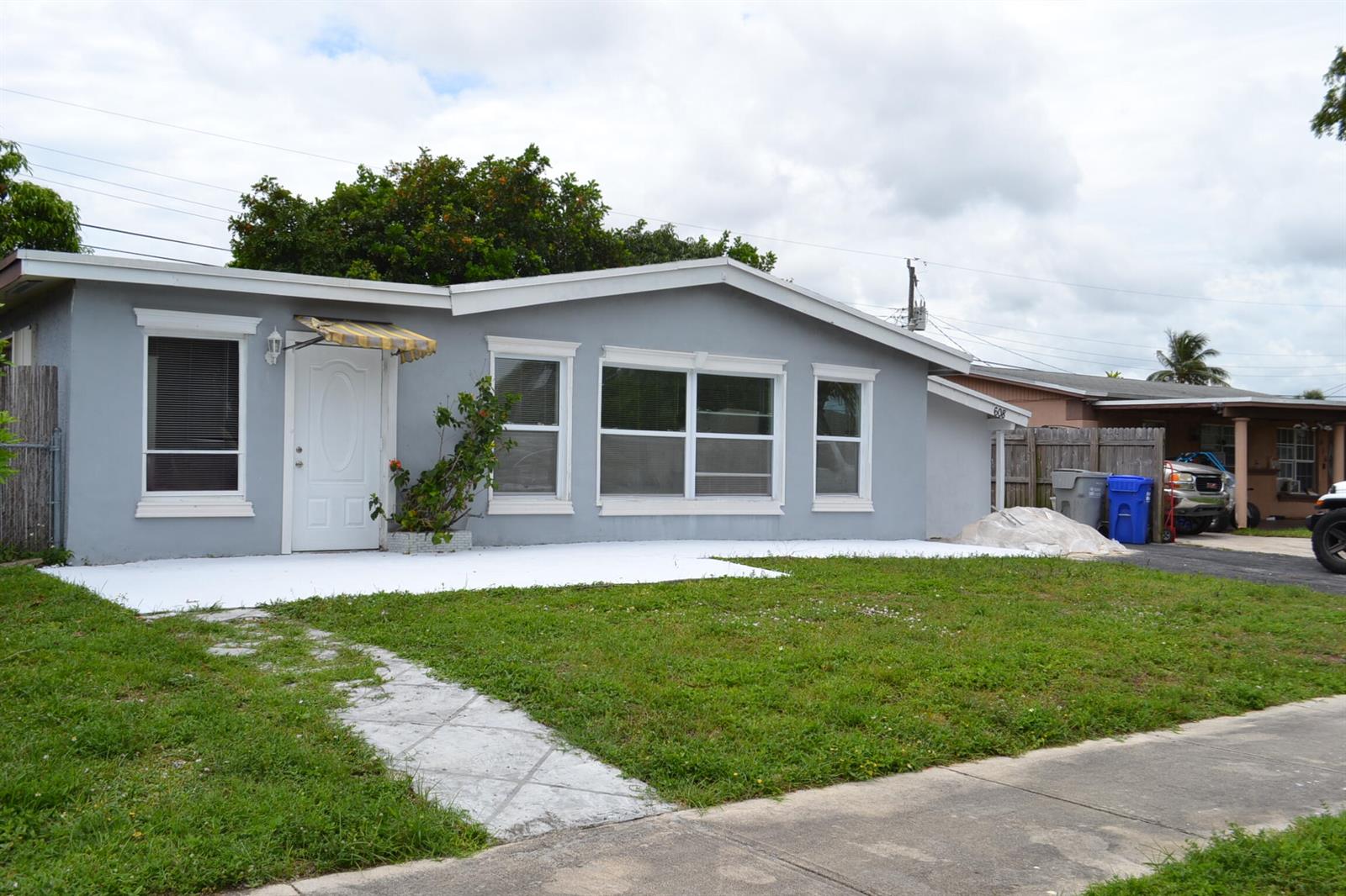 A single-story gray house with a white front patio, lawn, and a paved driveway — 608 NW 20th Court, Pompano Beach FL 33060, POMPANO BEACH, FL