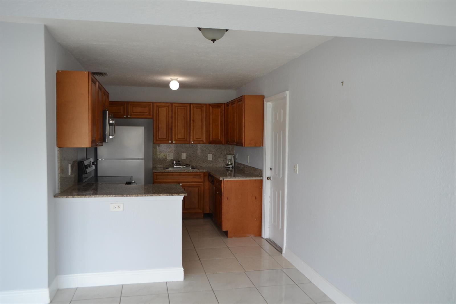 A kitchen features wood cabinets, granite countertops, and light-colored tile flooring — 608 NW 20th Court, Pompano Beach FL 33060, POMPANO BEACH, FL