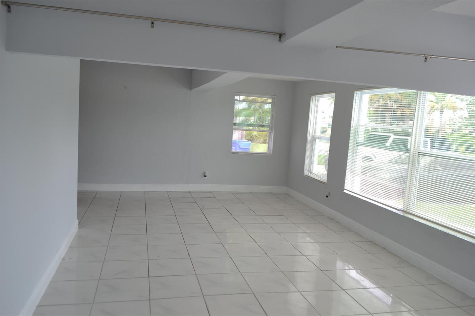 An empty room with white tile flooring, light gray walls, and several windows with blinds — 608 NW 20th Court, Pompano Beach FL 33060, POMPANO BEACH, FL