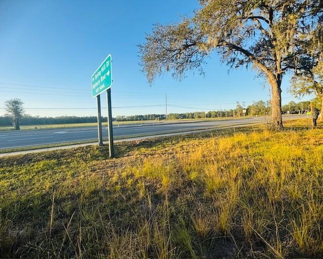 A road sign stands beside a paved highway near a large tree and grassy field — 17476 NICHOLAS AVENUE, BROOKSVILLE, FL