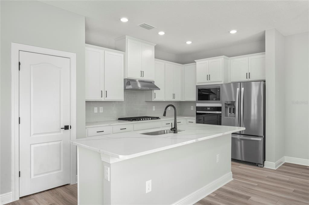 A modern kitchen features white cabinets, stainless steel appliances, a quartz island, and light flooring — 7813 MARLOW PLACE, KISSIMMEE, FL