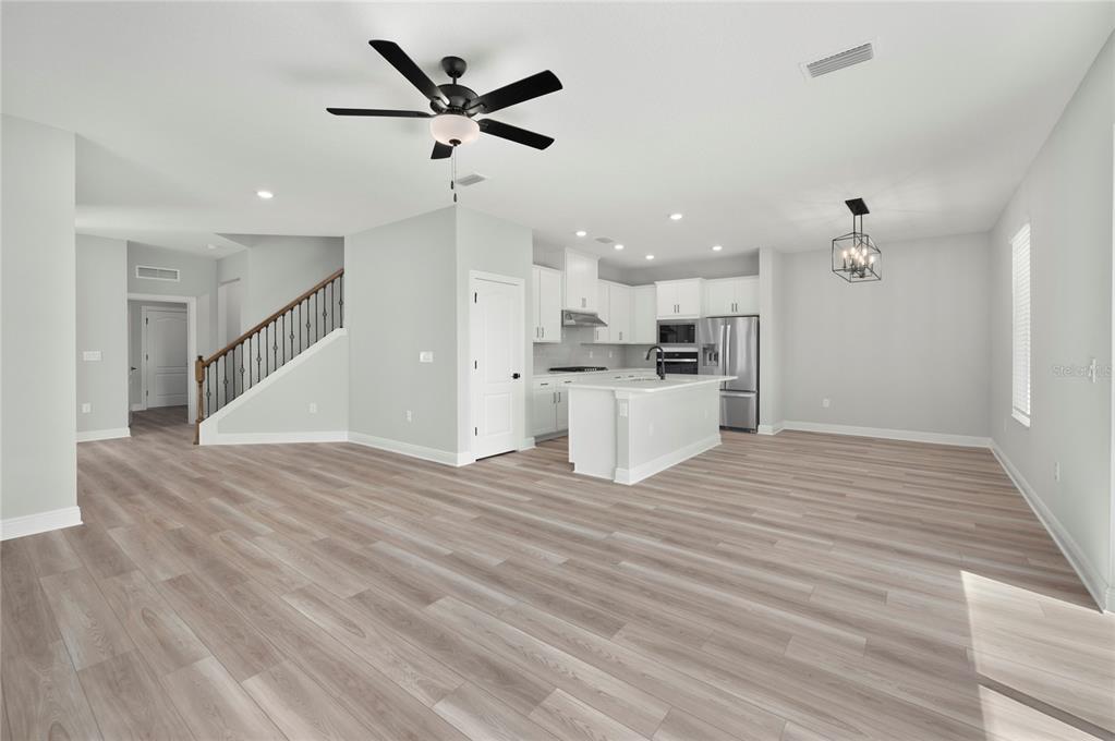An open-concept kitchen and living area features light wood-look flooring, white cabinetry, and a staircase — 7813 MARLOW PLACE, KISSIMMEE, FL