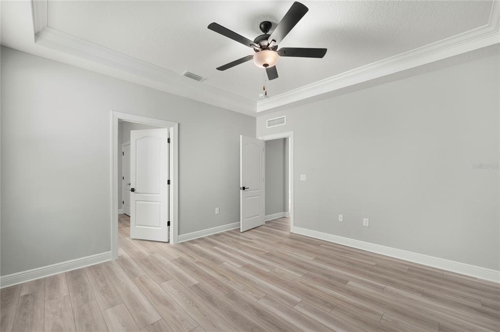 An empty bedroom features light gray walls, wood-look flooring, a tray ceiling, and a ceiling fan — 7813 MARLOW PLACE, KISSIMMEE, FL